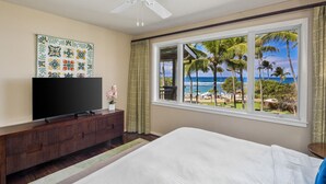 A bedroom with a large bed, a TV on a wooden cabinet, and a view of the ocean through a window.