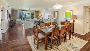A spacious dining area with a wooden table and chairs, a patterned rug, and a view of the ocean through large windows.