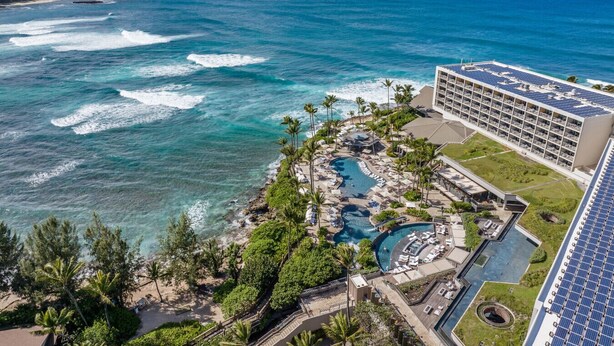A resort with multiple swimming pools, a beach area, and a building with solar panels.