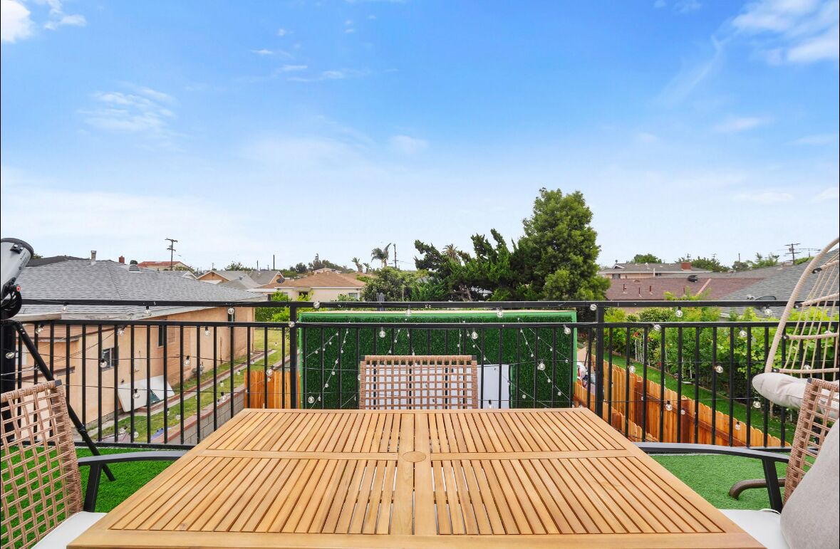 Une terrasse en bois avec une rambarde en métal, entourée d’une haie verdoyante et d’une clôture en bois.