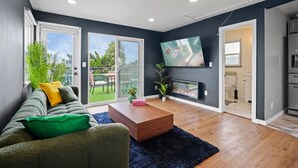Ein modernes Wohnzimmer mit Sofa, Couchtisch und Kamin. Ein Fernseher ist an der Wand montiert und eine Glastür führt auf einen Balkon.