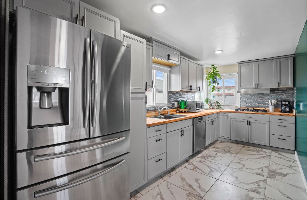A modern kitchen with stainless steel appliances, grey cabinets, and a marble floor.