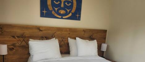 A hotel room with a large bed, wooden headboard, two bedside tables with lamps, and a wall decoration.
