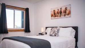 Une chambre d’hôtel avec un lit, une fenêtre avec des rideaux, une table de chevet avec une lampe et un tableau représentant des chevaux accroché au mur.