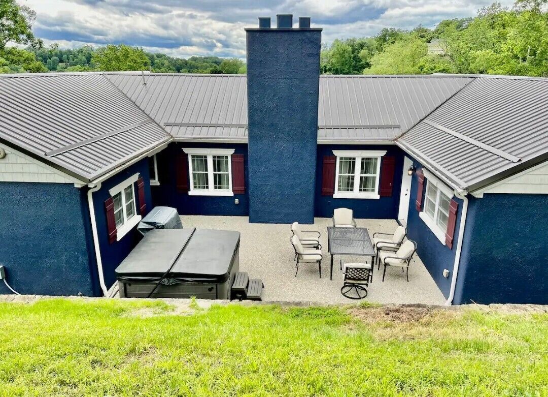 A two-story building with a central chimney, outdoor seating area with tables and chairs, and a grassy yard.
