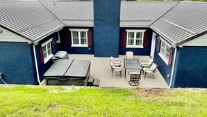 Ein zweigeschossiges Gebäude mit einem zentralen Schornstein, einer Außenbereich-Sitzgelegenheit mit Tischen und Stühlen sowie einem Rasenplatz.