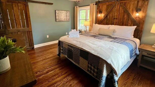 Ein Schlafzimmer mit einem Bett, Holzboden, einer Kristallleuchter, einer Pflanze und einer Schiebetür im Bauernhausstil.