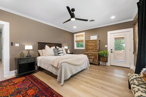 A bedroom with a bed, bedside tables, a ceiling fan, a dresser, a window with blinds, and a door. - Luxe in Lampasas 1920's home, pool, hot tub, private cabana with massage chair. (Lampasas)
