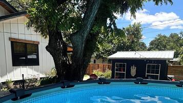 Une piscine dont le fond est recouvert de carreaux, entourée d’arbres et de bâtiments.