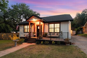 A two-story house with a front porch, a mailbox, and a small garden. - Luxe in Lampasas 1920's home, pool, hot tub, private cabana with massage chair. (Lampasas)