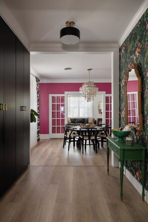 Un coin repas agrémenté d’un lustre, d’une table avec des chaises et d’une console verte ornée d’un miroir.