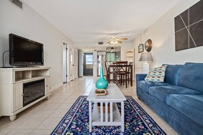 A living room with a television, a blue sofa, a white coffee table, and a patterned rug. - The Hudson Resort On The Gulf (Hudson)