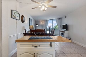 A dining area with a wooden table, chairs, a ceiling fan, a television, and a view of the outdoors. - The Hudson Resort On The Gulf (Hudson)