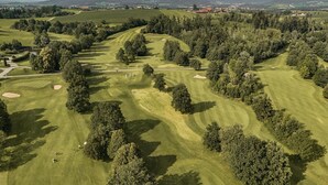 An aerial view of a golf course with rolling hills, trees, and distant buildings.