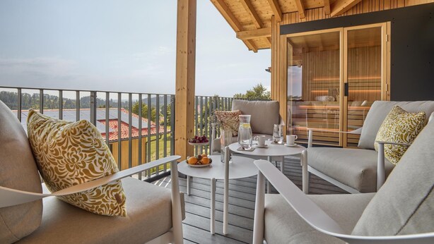 A balcony with a view of solar panels, a table with glasses and a pitcher, and two sofas with patterned cushions.