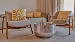 A living room with two wooden chairs, a textured coffee table, and a sofa with yellow pillows.