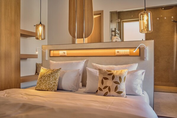 A modern bedroom with a large bed, bedside lamps, a mirror, and a wooden headboard.