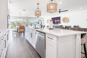Una cocina moderna con una isla grande, luces colgantes y vistas a una piscina.