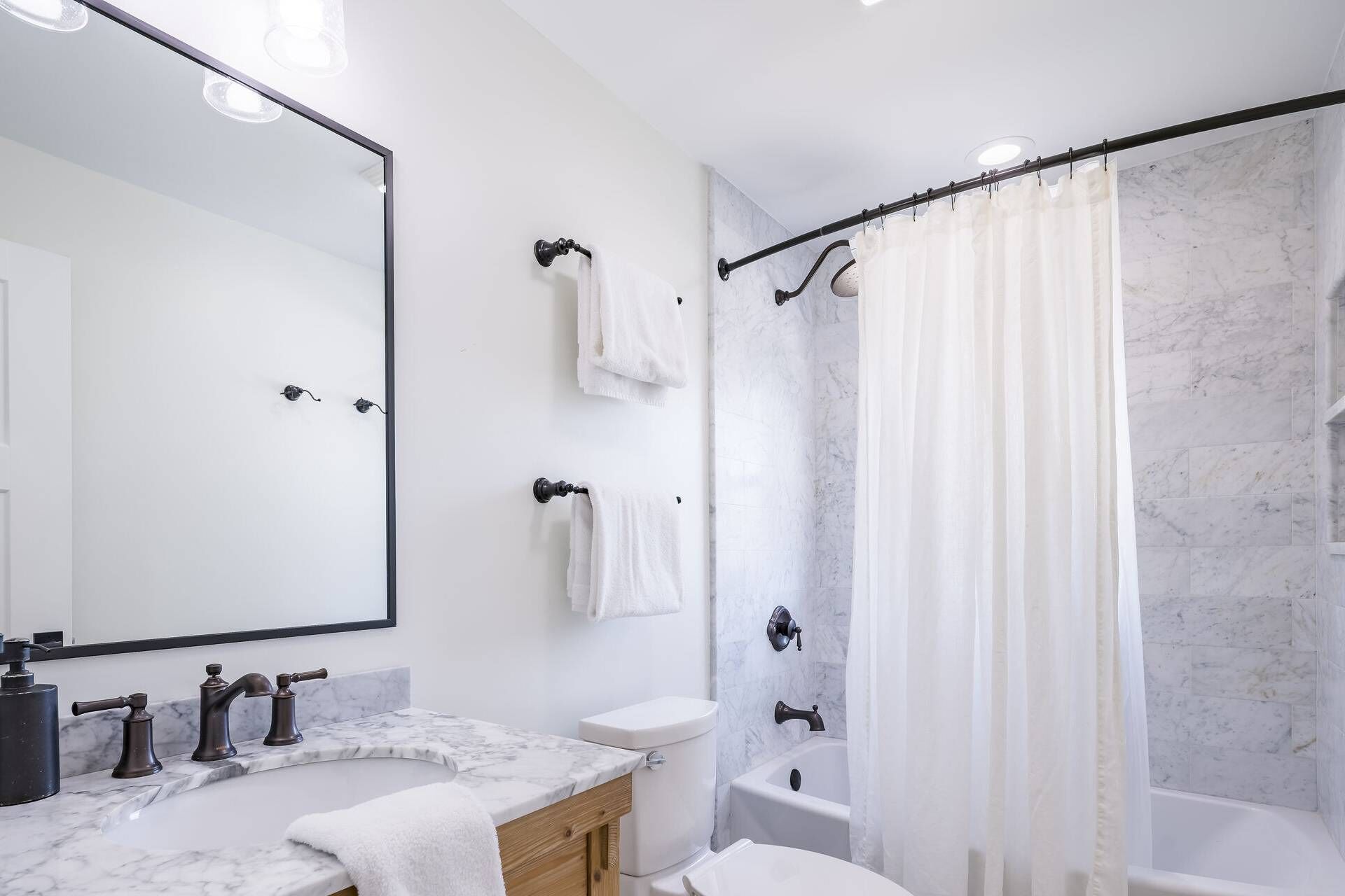 Ein modernes Badezimmer mit Marmorwaschbecken, Toilette, Badewanne und Duschvorhang.