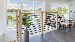 Une pièce dotée de grandes fenêtres donnant sur un port de plaisance, d’une cloison en bois avec des barreaux métalliques et d’un coin repas avec des chaises et une table.