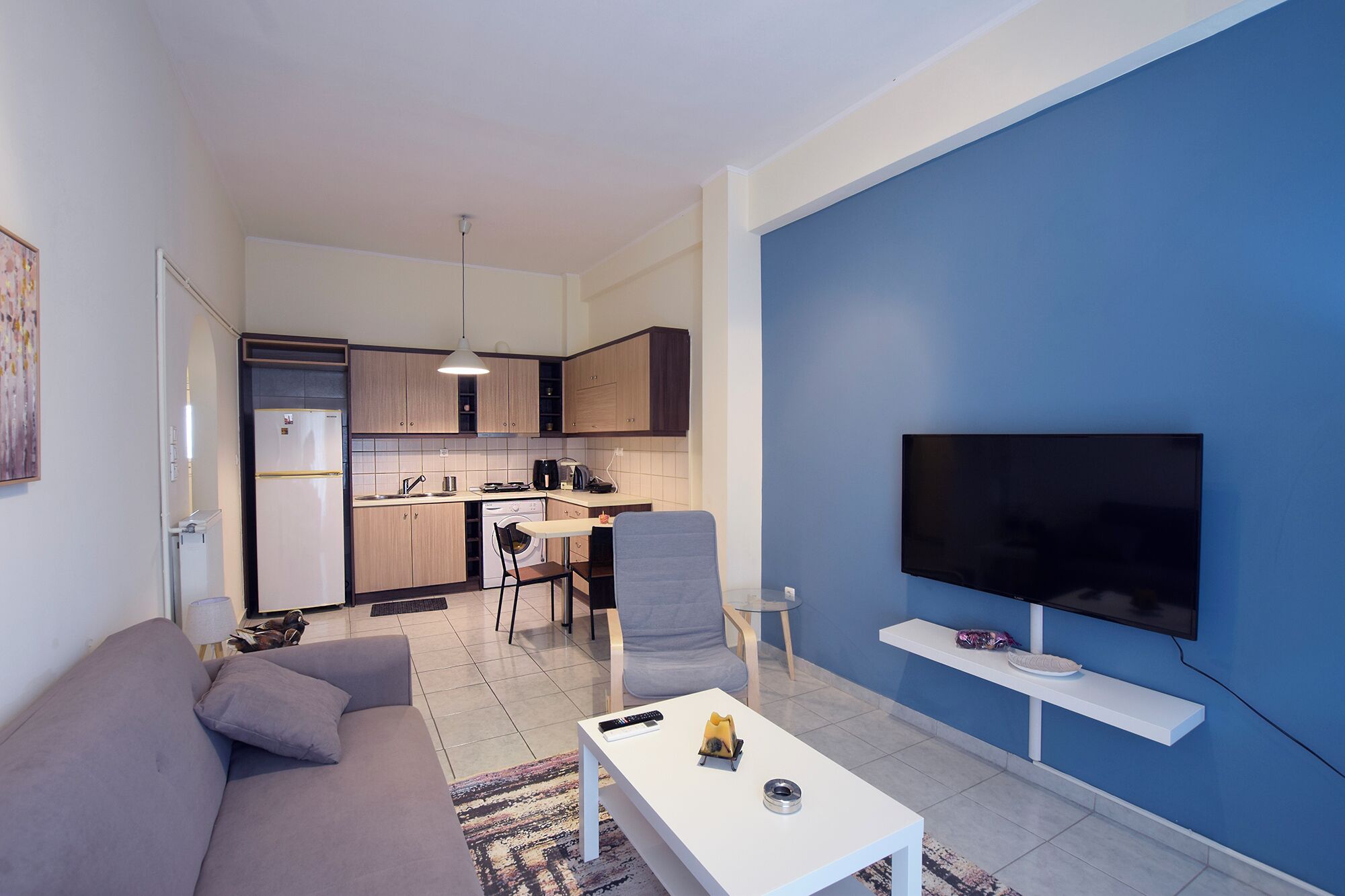 A modern living room with a sofa, coffee table, and a TV mounted on a blue wall.