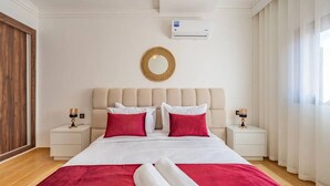 Een hotelkamer met een bed, twee nachtkastjes, een wandairconditioner, een houten deur en een raam met gordijnen.
