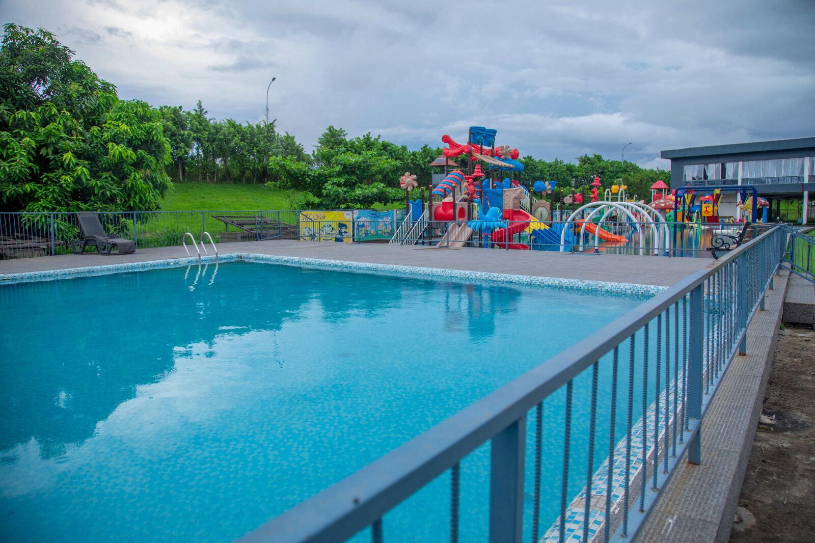 Una piscina con uno scivolo e strutture giochi sullo sfondo.