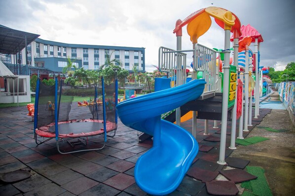 Un parque infantil con un tobogán azul, un trampolín y una estructura para escalar.