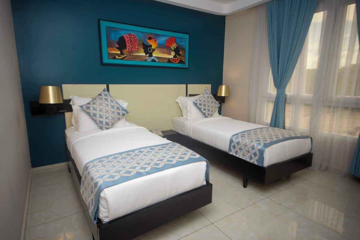 Two single beds with headboards, a painting on the wall, and a window with curtains.