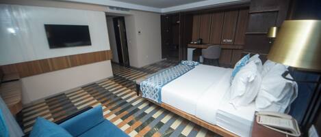 A hotel room with a bed, a desk, a chair, a TV, and a patterned floor.