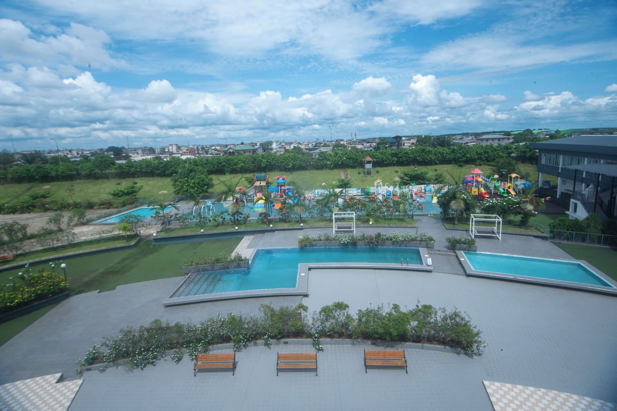 A rooftop pool area with multiple swimming pools, benches, and a view of the surrounding landscape.