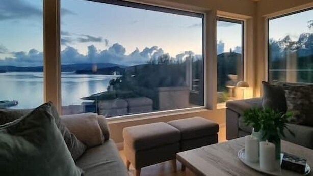 Un salon moderne doté de grandes fenêtres, d’un canapé, d’une table basse et offrant une vue sur un lac et des montagnes.