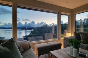 Un salon moderne doté de grandes fenêtres, d’un canapé, d’une table basse et offrant une vue sur un lac et des montagnes.