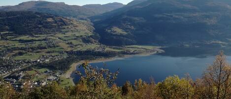 A panoramic view of a valley with a lake, surrounded by hills and trees.