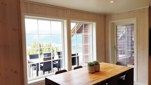 A dining area with a wooden table and chairs, large windows with a view of trees and mountains, and a potted plant on the table.