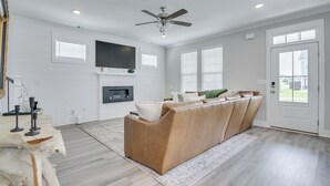 A living room with a sofa, a ceiling fan, a flat-screen TV, and a door. - Masters/ANWA Rental Retreat (Grovetown)