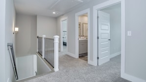 A hallway with a staircase, white walls, and a kitchen area visible through an open door. - Masters/ANWA Rental Retreat (Grovetown)