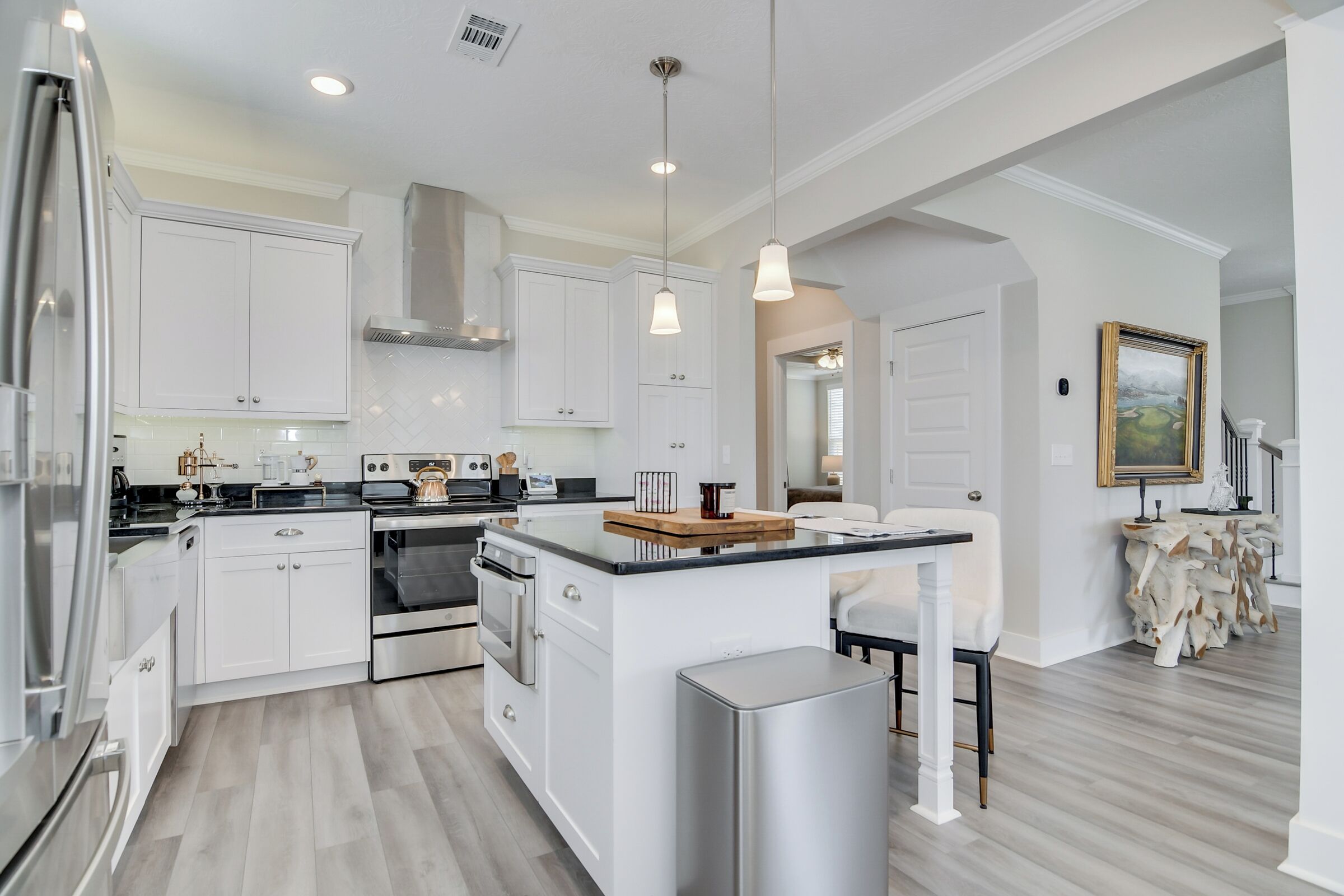 A modern kitchen with white cabinets, stainless steel appliances, and pendant lighting.
