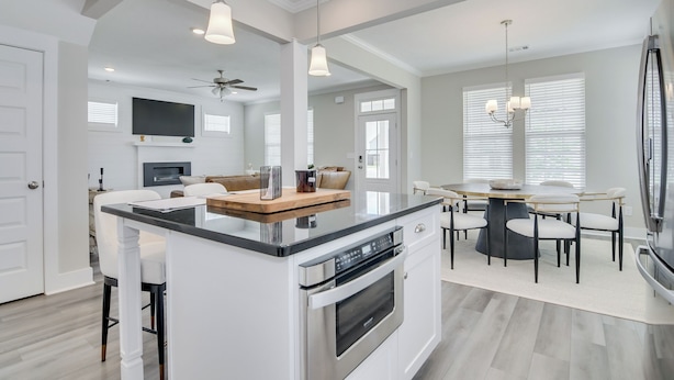 A modern kitchen with a central island, a dining area with a round table, and a built-in TV. - Masters/ANWA Rental Retreat (Grovetown)