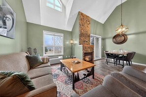 A spacious living room with a fireplace, a dining area, and a view of the outdoors. - Top Floor with Loft | Pool | Mountain Views (NEW LISTING!) (Radium Hot Springs)