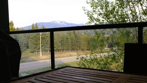 Une table en bois, une tasse, une vue sur une route et une forêt avec des montagnes à l’horizon.