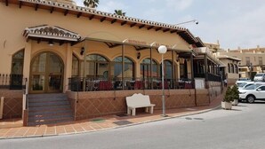 Un restaurante con fachada de azulejos, ventanas en arco y un área de estar al aire libre cubierta.