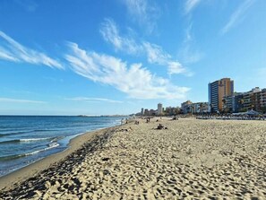 A wide sandy beach with a calm sea, a clear sky, and buildings in the background. - Exclusive 2 bedroom apartment, 100m from beach (Fuengirola)