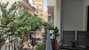 Un balcón con vistas a una calle estrecha bordeada de edificios, una planta en maceta y una silla.