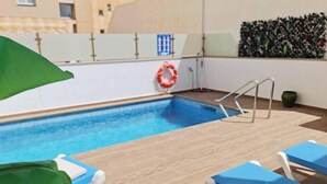 Un área de piscina en la azotea con agua azul, un flotador salvavidas y sillas de descanso azules.
