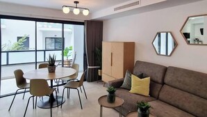 Una sala moderna con un sofá, una mesa de comedor con sillas, un ventanal grande y una lámpara en el techo.