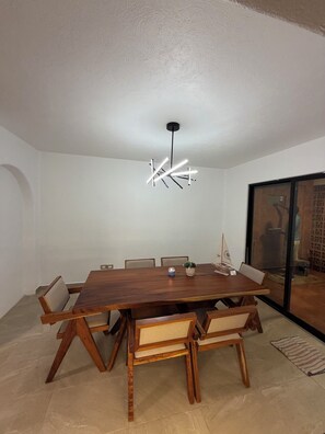 A dining area with a wooden table, chairs, a modern light fixture, and a view through a glass door.