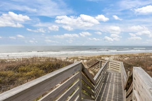 Een houten looppad dat naar een strand leidt, met een heldere lucht en uitzicht op de oceaan.