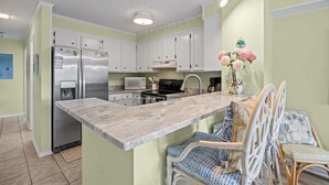 A kitchen with white cabinets, a marble countertop, and a dining area with wicker chairs. - Island Beach and Racquet Club B104: Oceanfront Condo with Views, Community Amenities (Atlantic Beach)
