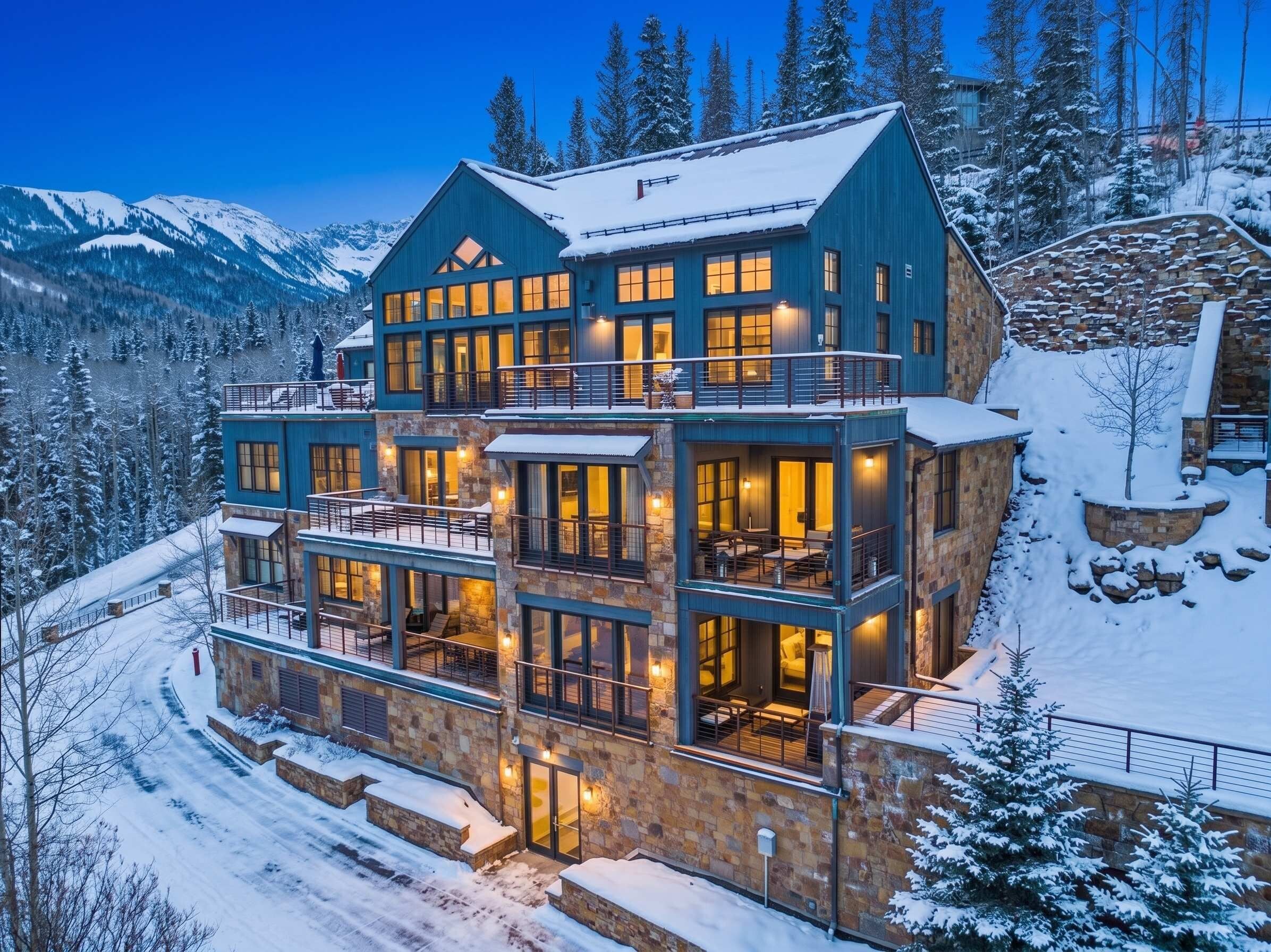 A multi-story lodge with a stone facade, multiple balconies, and a view of snow-covered mountains.